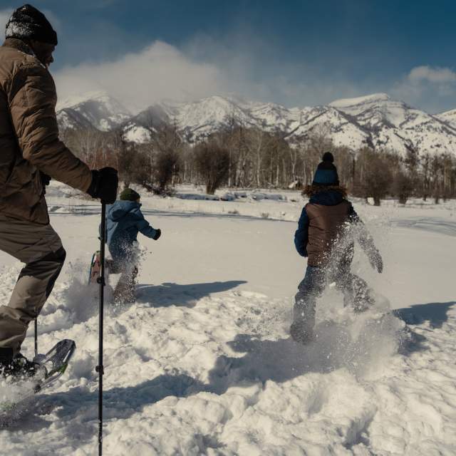A group snowshoes through deep powder near Jackson, Wyoming, with snow-covered mountains rising across the horizon. The winter landscape and fresh snow highlight family-friendly snowshoeing and outdoor recreation in Teton County.
