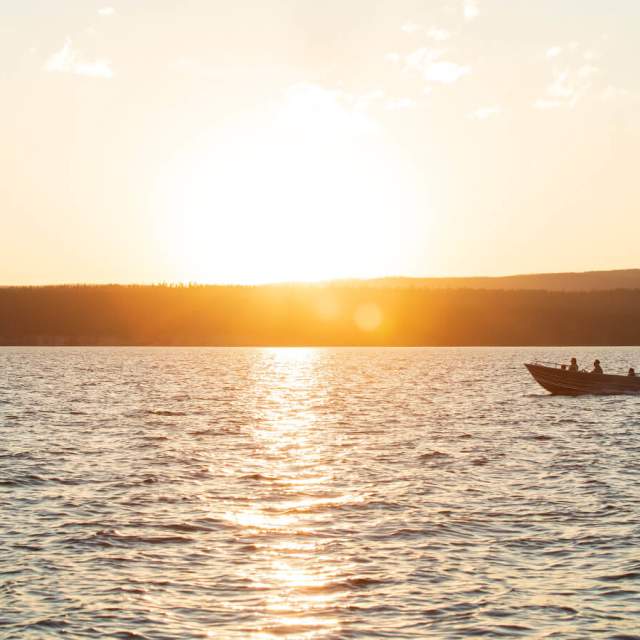 Persons boating on a calm lake at sunset surrounded by scenic mountains in Wyoming.