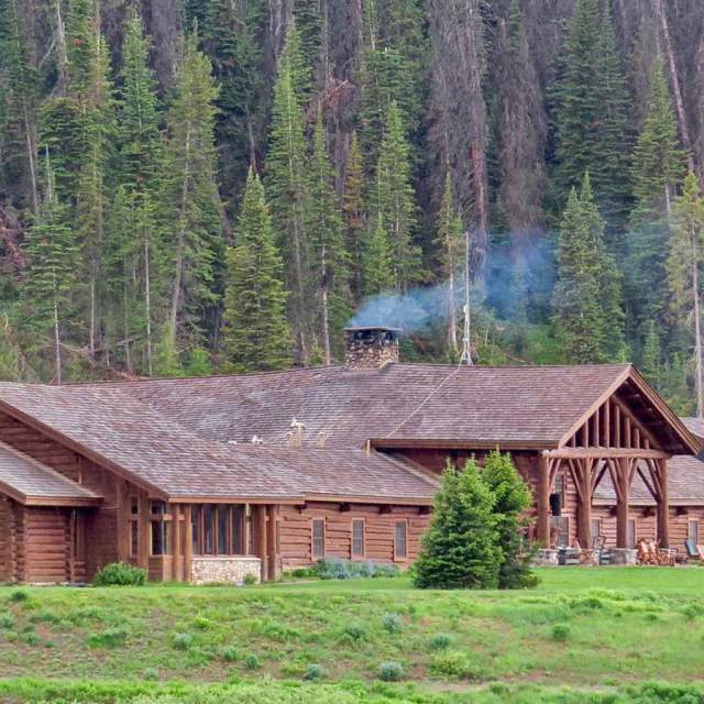 Lodge with smoke rising from fireplace in forest.