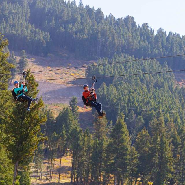 Riders soaring on a zipline over snowy landscapes at Snow King Mountain in Wyoming.