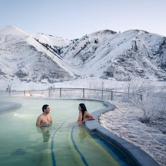 Steam rising from a natural hot spring with people soaking surrounded by snowy landscapes at Astoria Hot Springs Park in Wyoming.