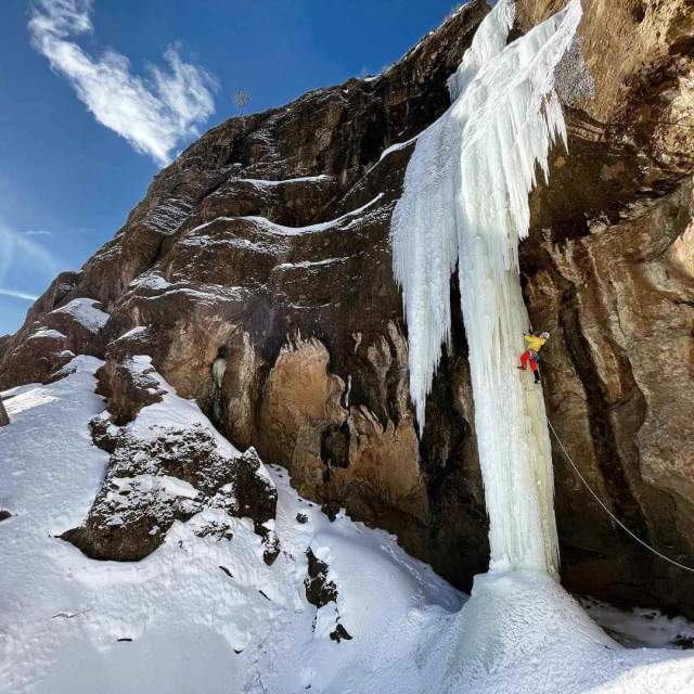 Ice climber scaling frozen waterfall against mountain.