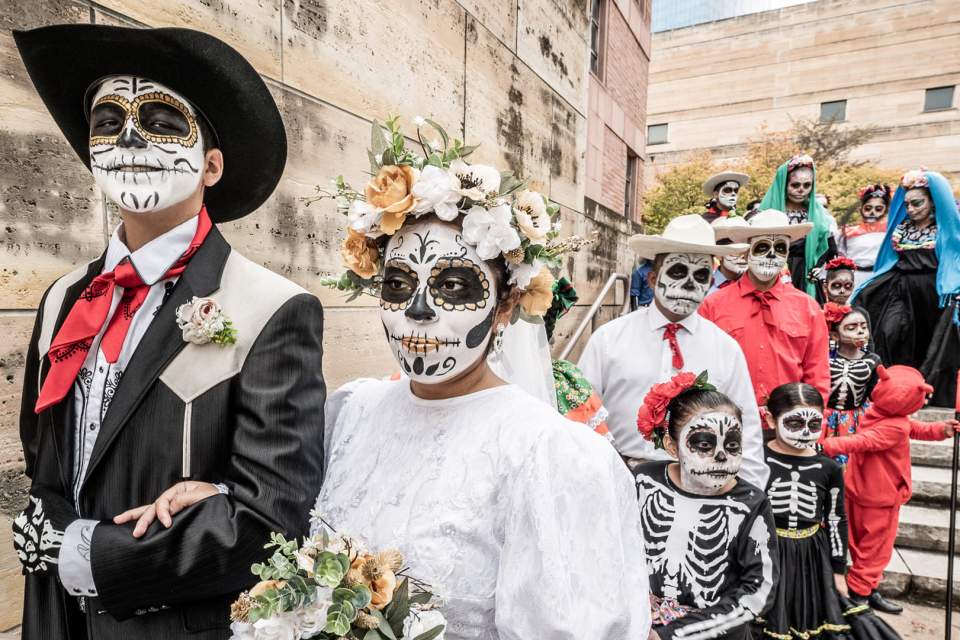 A group of people in skeleton costumes gather for a parade outside the Eiteljorg Museum