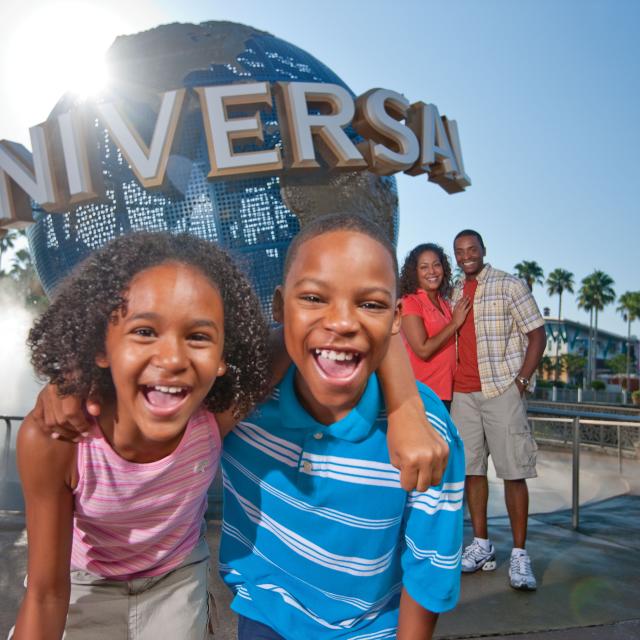 A brother and sister hug in front of the globe, while their parents smile together in the background at Universal Studios Florida
