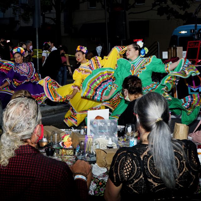 Dancers performing outdoors as a small crowd watches.