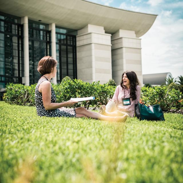 Two women sitting in the grass outside of the Orlando/Orange County Convention Center West Building