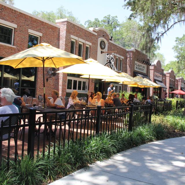 People sitting and drinking under umbrellas in outdoor dining area of Crooked Can Brewing Company at Plant Street Market in Winter Garden.
