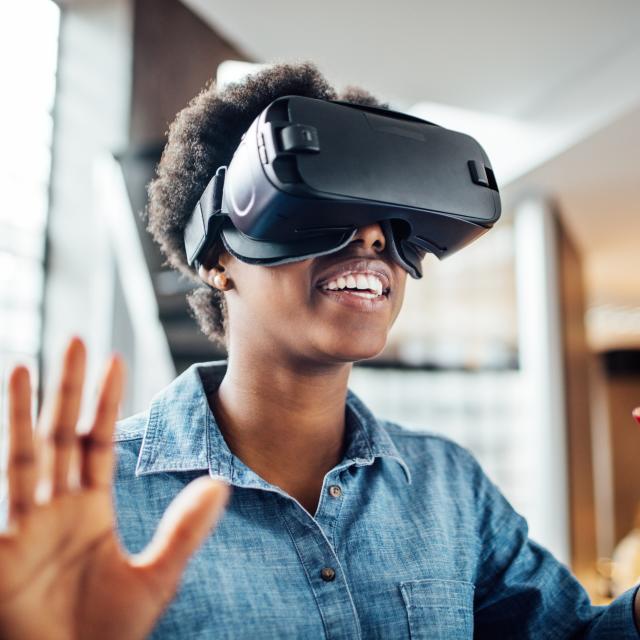 Smiling african-american woman wearing virtual reality headset in office. Young female at startup using VR goggles.