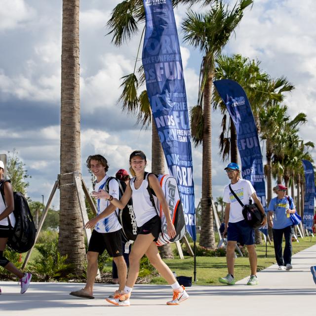 Tennis players walking along the palm tree-lined sidewalk at USTA National Campus