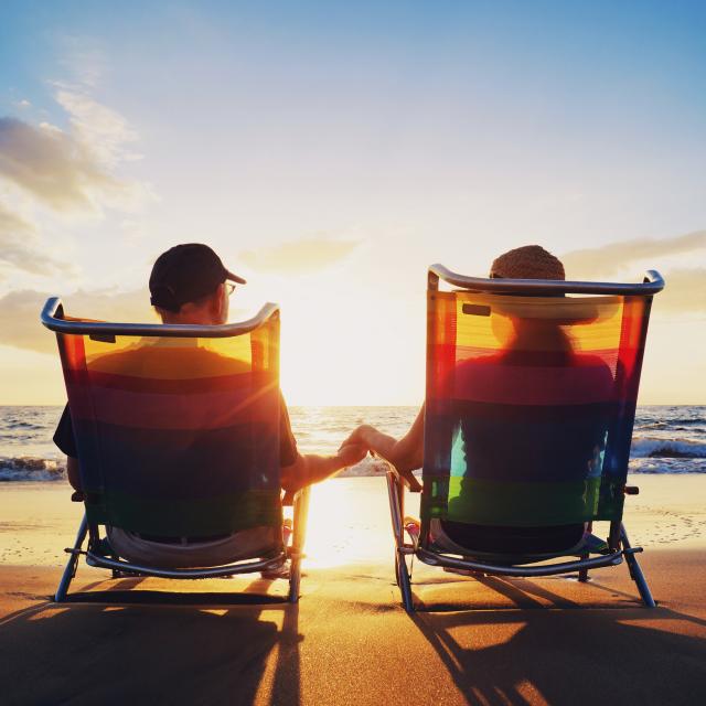 A senior couple sitting on the beach holding hands and watching the sunset