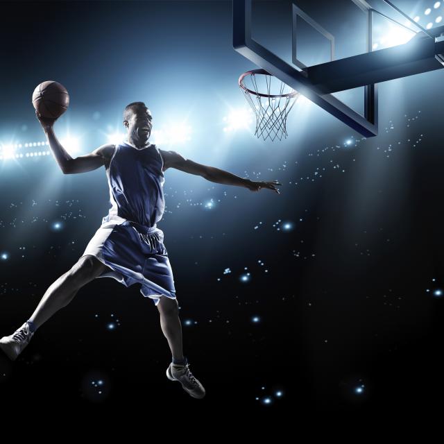 A male basketball player, in the air, ready to dunk the ball