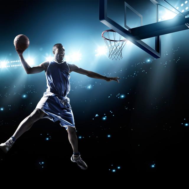 A male basketball player, in the air, ready to dunk the ball
