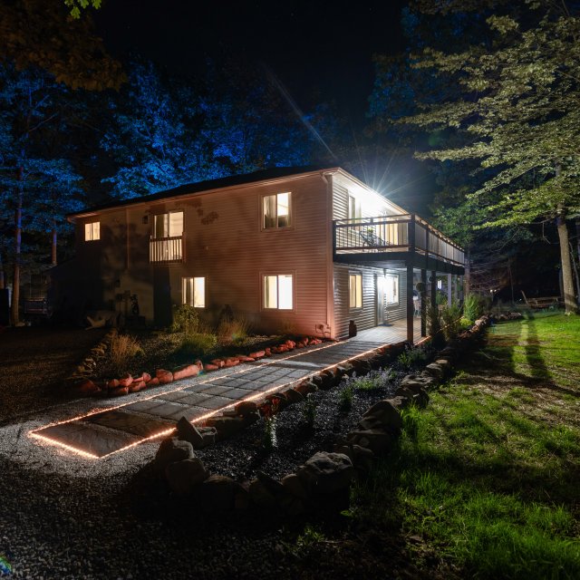 Exterior view of a vacation rental at night with a lit walkway leading to the house and lights glowing inside.