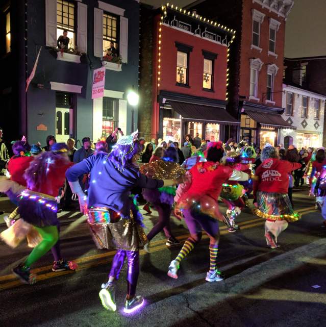 People in bright colors wearing light up shoes and other lights in the Mainstrasse Village Mardi Gras parade