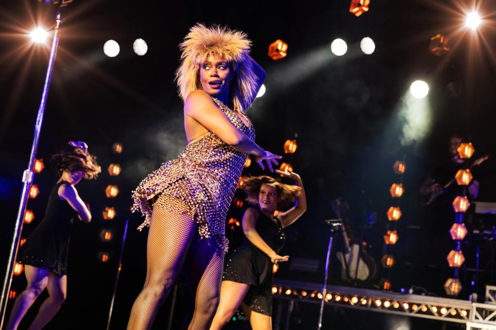 Darilyn Burtley as Tina on a dark stage with lights around her.