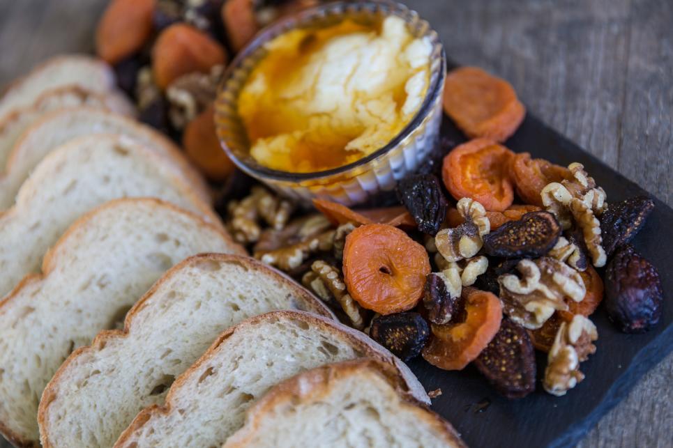Sliced bread and dried fruits and nuts and a bowl of butter spread are arranged on a platter.