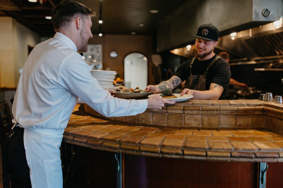 A cook passes a plate to a server over the bar at Marche.