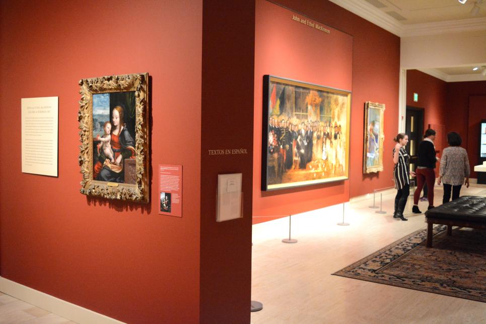 The red, art covered walls of a museum with viewers in the background.