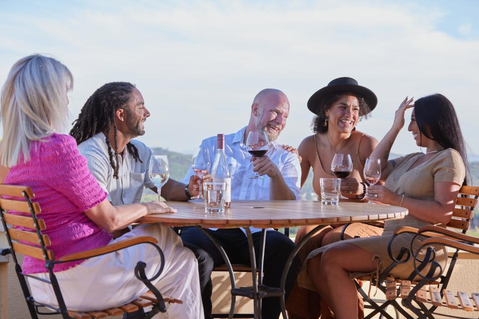 A group of people sit around a table sipping wine.