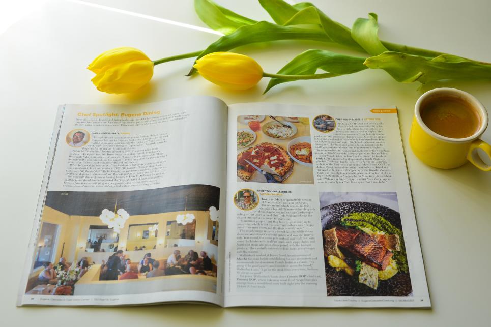 The visitor guide magazine is open next to a cup of coffee in a yellow mug and some yellow tulips.