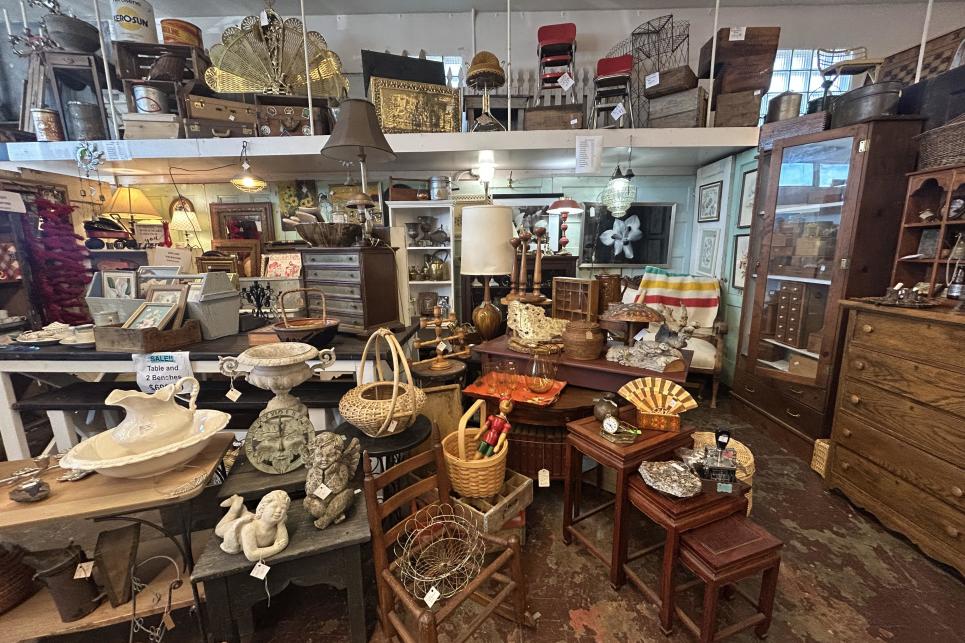 A crowded antique store piled high with baskets and pottery, and along a top high shelf, even more!
