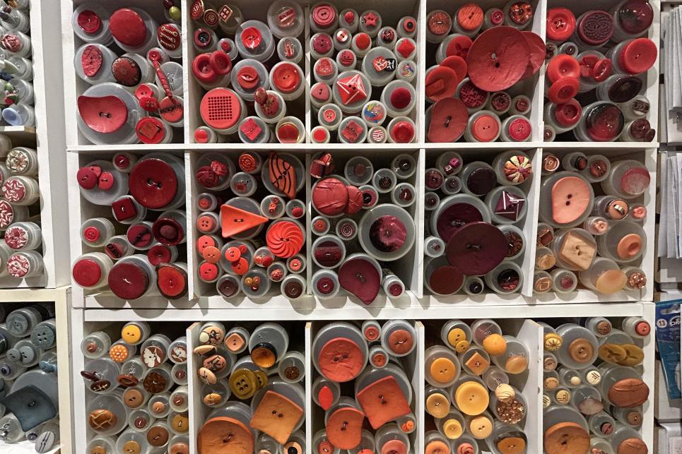 A large display of buttons of a variety of shapes and sizes organized by color, in this picture yellows, oranges and reds.