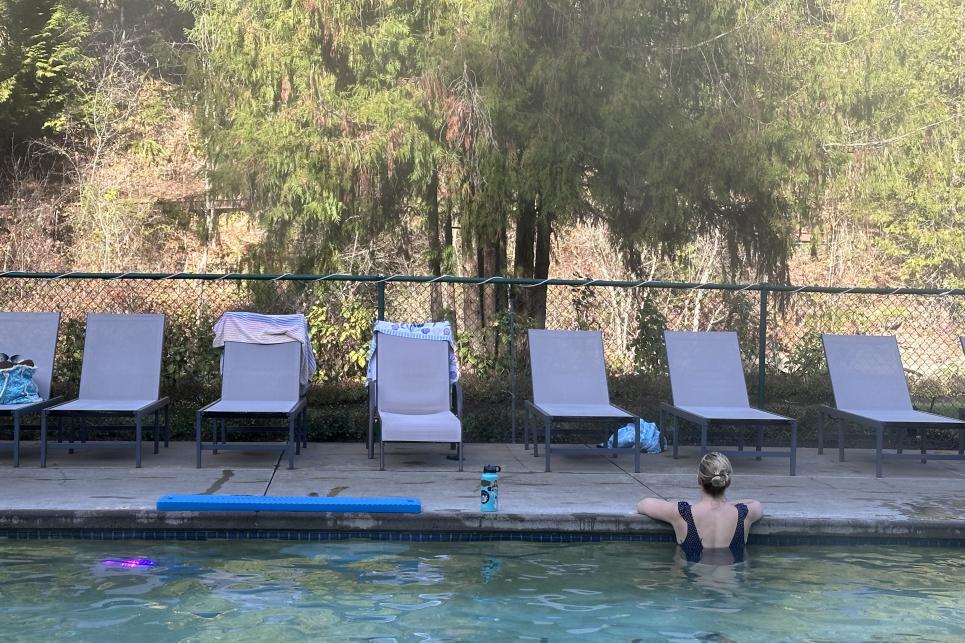 A woman stands in the hot spring's water looking toward the river.