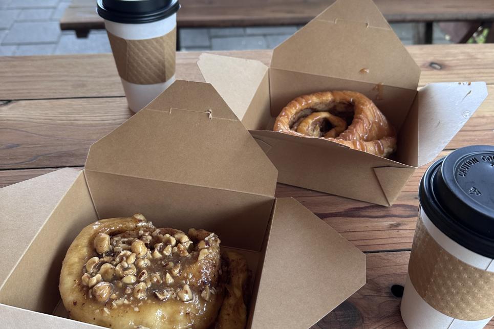 Sticky rolls in paper to go boxes and to go hot drink beverages on a picnic table.