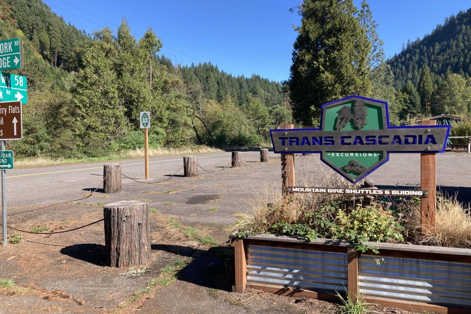 The Trans Cascadia sign in a planter box with stumps marking off the parking lot boundaries.