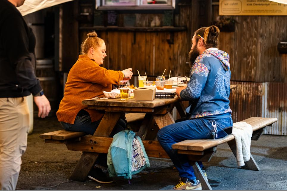 Two people sit at a picnic table eating fare from a food truck.
