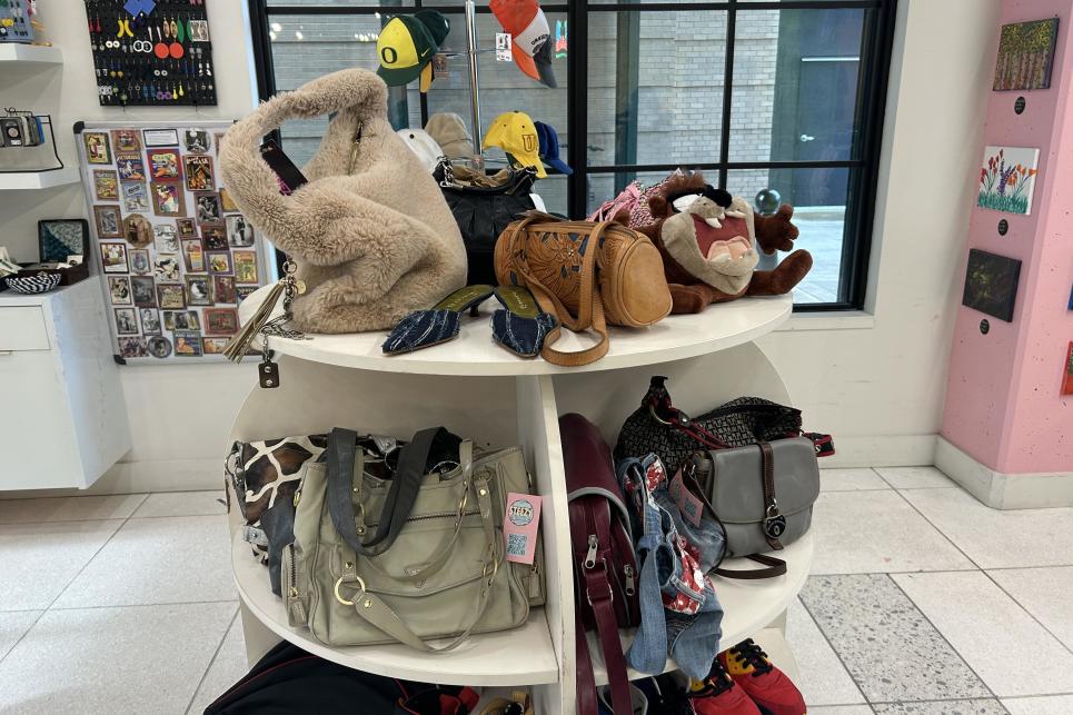 A round table with shelves displays a variety of handbags in the middle of the store.