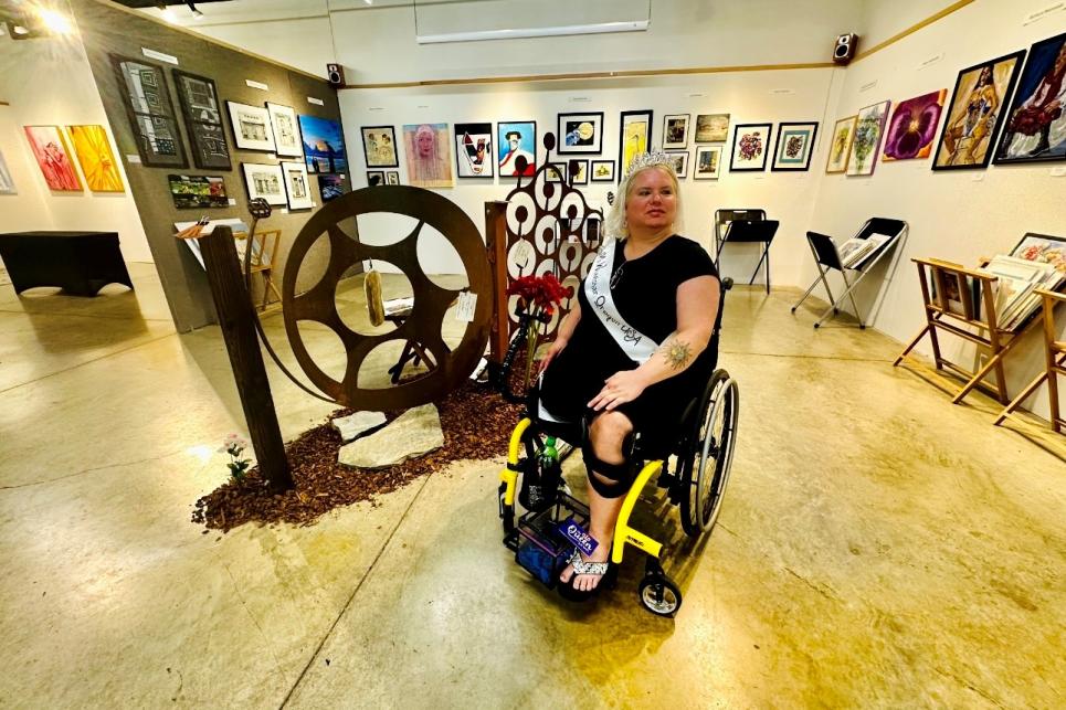 Melinda with her Ms. Wheelchair sash poses in front of art work.