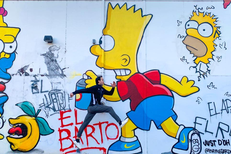 A man jumps in front of a mural of characters from the television show The Simpsons.