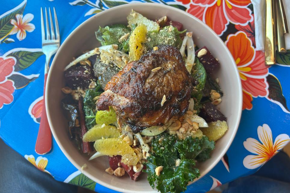 Top down view of a green salad with citrus and chicken on a floral table cloth.
