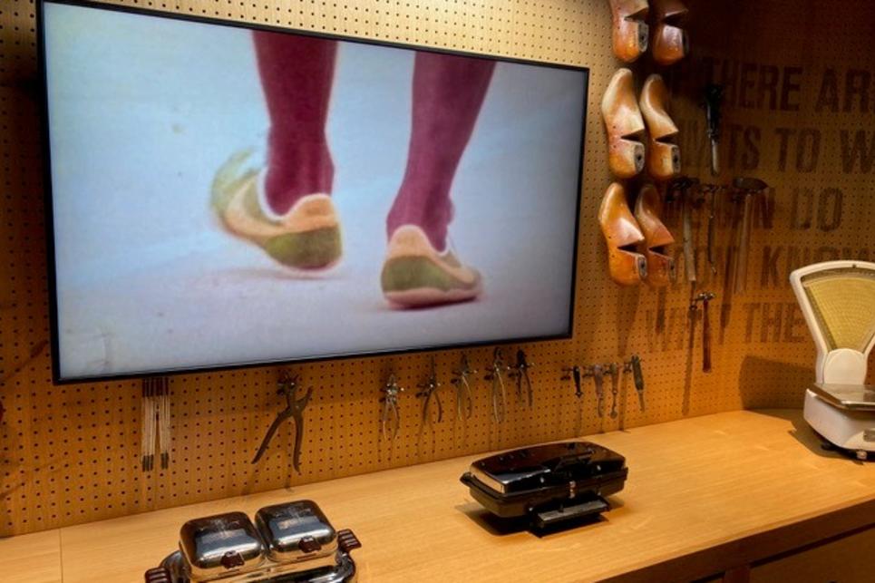 A TV screen shows shoes above a counter with waffle irons on it.