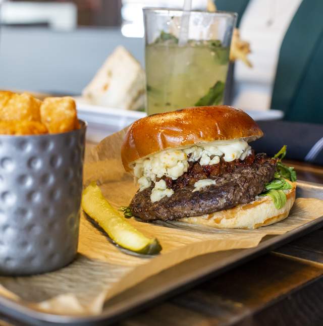 Black ad Bleu burger with a pickle spear and cajun tator tots