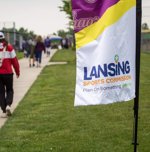 The Lansing Sports Commission flag with athletes walking to the field