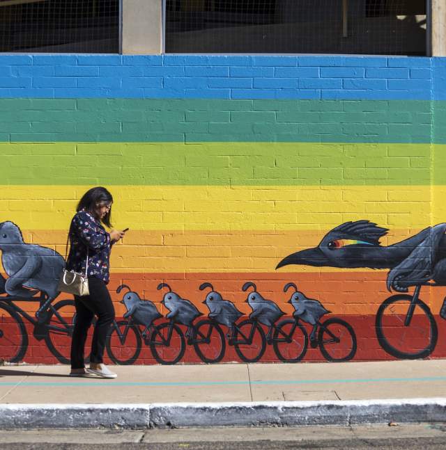woman walking in front of a rainbow mural with Quails on bikes