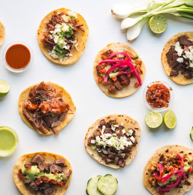 Tacos and garnishes (salsas, pepinos, limes, onions)