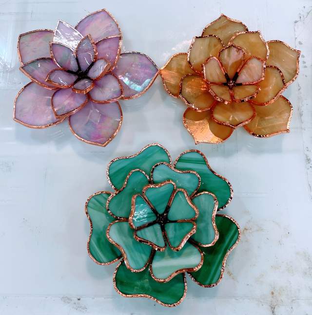 Three different colored stained-glass plants sit on a marble background