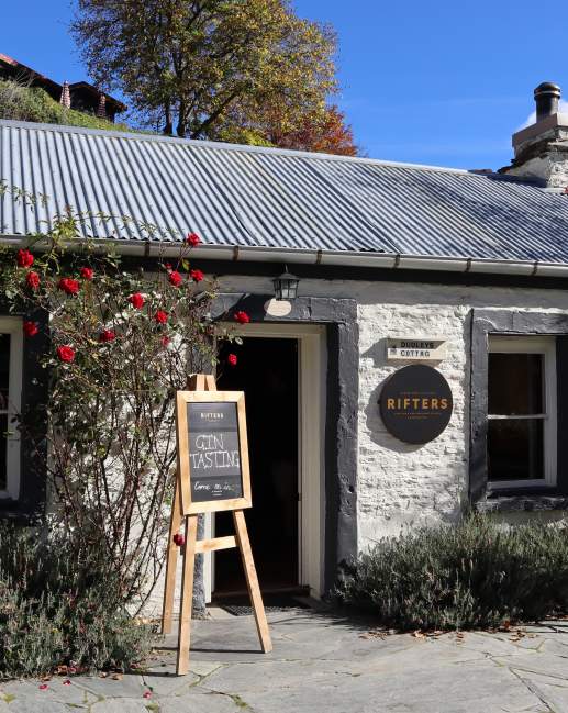 The outside of a white brick cottage with signs out the front for gin tasting