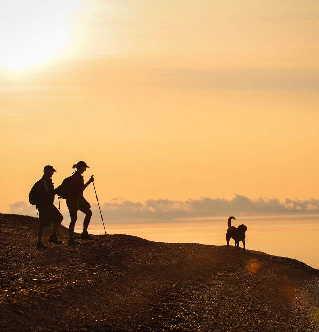 Two people hiking the beach with a dog next to Lake Superior