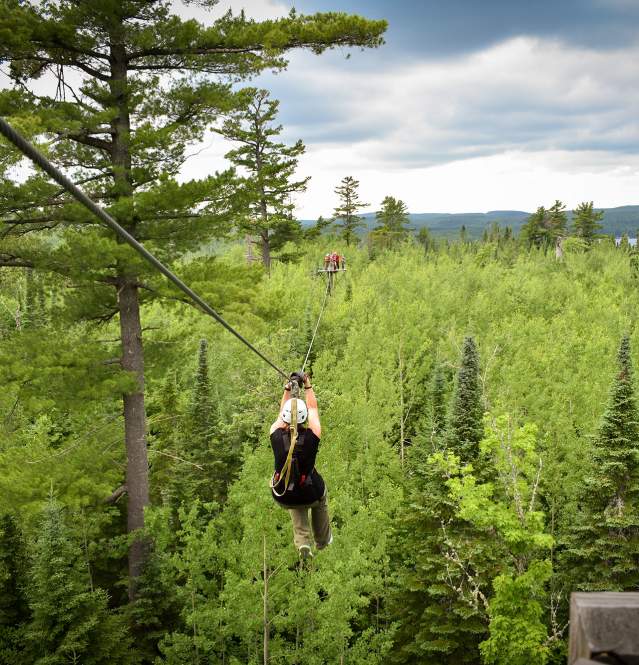 Female ziplining through the woods with lake views