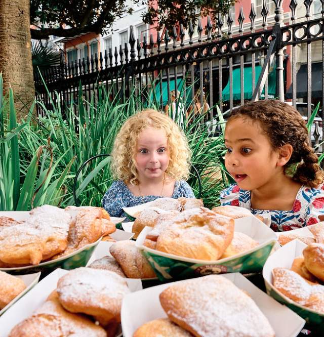 Two Children sit in front of a table of $100 of Beignets at Cafe Beignet in New Orleans' French Quarter.