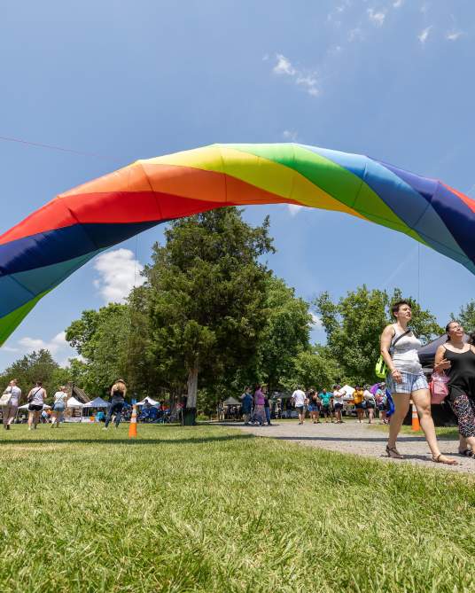 Attendees walk under a large rainbow arch at an outdoor Pride festival in Loudoun County, Virginia
