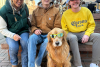 Three people posing with a dressed up and in sunglasses golden retriever at Goldens in Golden CO event 2025
