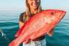 A woman in a boat holding a freshly caught Red Emporer