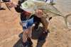 A child holding a Trevally, freshly caught from the shore at Port Hedland. A man crouches behind the child, supporting him