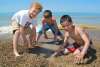 Three young boys play in the sand near the shoreline