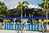 Rendering of people walking in front of swing ride and palm trees.